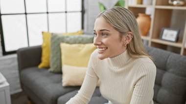 Hoş bir oturma odasında gülümseyen sarışın kadın modern iç tasarım sergiliyor.