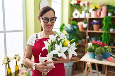 Young beautiful hispanic woman florist holding bouquet of flowers at flower shop