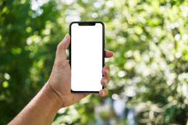 Akıllı telefonu tutan adam parkta beyaz ekranı gösteriyor.