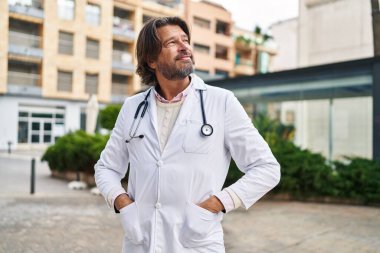 Orta yaşlı doktor sokakta kendine güvenen gülümsüyor.