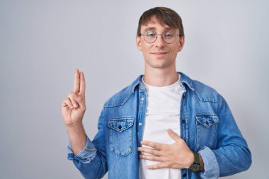 Beyaz, sarışın, gözlüklü, gülümseyen, elleri göğsünde, parmakları havada yemin eden, sadakat yemini eden bir adam. 