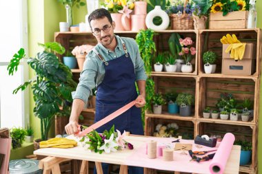 Young hispanic man florist smiling confident holding gift lace at flower shop