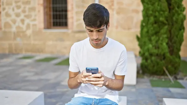 公園で真剣な表情のスマートフォンを使っている若いヒスパニック系の男 — ストック写真