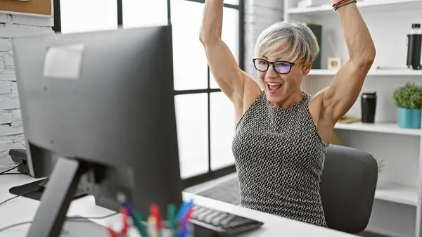 灰色の髪を持つ楽しい成熟した女性は 彼女のオフィスワークスペースで成功を祝います — ストック写真