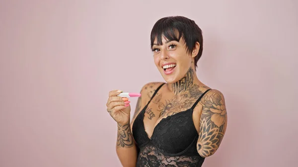 Hispanic woman with amputee arm wearing lingerie looking pregnancy test smiling over isolated pink background