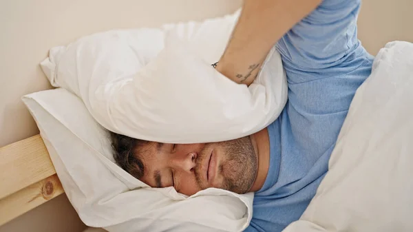 Young hispanic man covering ears for noise at bedroom