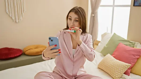 居心地の良い寝室でセルフィーを服用しながら妊娠テストをチェックするパジャマのブルネット女性 — ストック写真