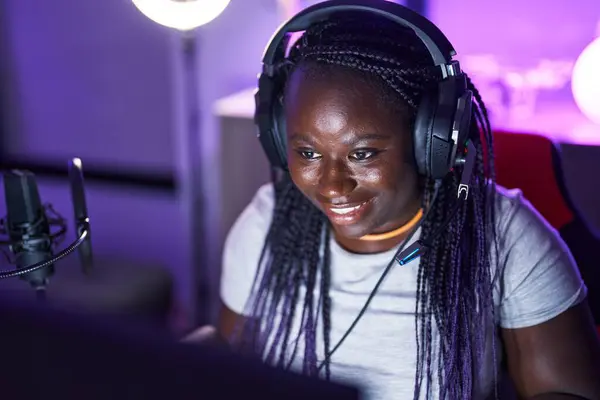 African american woman streamer playing video game using computer at gaming room