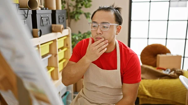 Intricate thoughts of a young chinese artist, engrossed in the art of drawing, dressed in an apron and glasses at his cozy studio