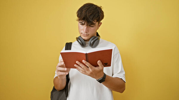 Крутой молодой латиноамериканец, сфокусированный студент-мужчина, погруженный в увлекательную книгу, стоя на поразительно изолированном желтом фоне