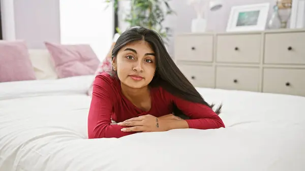 stock image A beautiful south asian woman lies on a bed, her long hair and serene expression adding charm to the cozy bedroom setting.