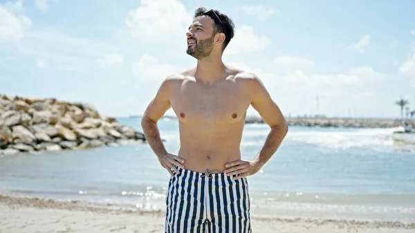 Young hispanic man tourist smiling confident wearing swimsuit at the beach