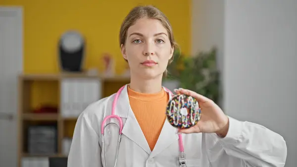 Young Blonde Woman Dietician Holding Doughnut Serious Face Clinic — Stock Photo, Image
