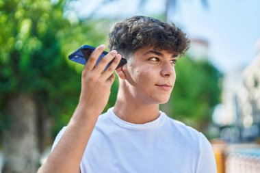 Genç İspanyol genç gülümsüyor. Parktaki akıllı telefondan kendine güvenen bir sesli mesaj dinliyor.