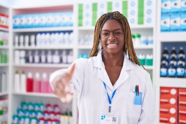 Afro-Amerikalı kadın eczacı gülümseyerek eczanede el sıkışıyor.