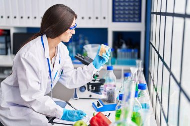 Genç ve güzel İspanyol bilim kadını elinde makarna ile laboratuvarda yazı yazıyor.