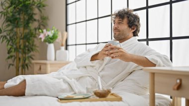 Bornoz giyen genç İspanyol adam yatak odasında bir fincan kahve tutuyor.