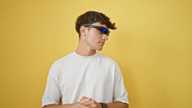 Siber-bilgili İspanyol genç, oyuna dalmış, VR gözlüklerini takmış, destansı bir gelecek oyunu oynuyor, hepsi havalı ve konsantre, canlı sarı bir arka planda tek başına duruyor..