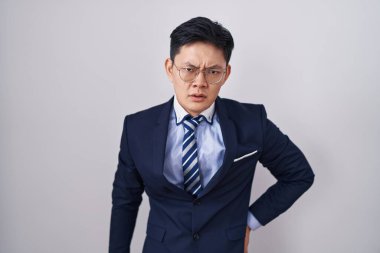 Asyalı genç bir adam iş elbisesi ve kravat takmış, şaşkın ve alaycı görünüyor, ağzı açık kalınca şaşırıyor. 