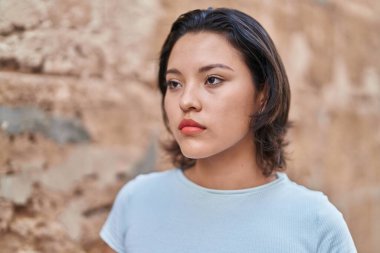 Young hispanic woman looking to the side with serious expression at street