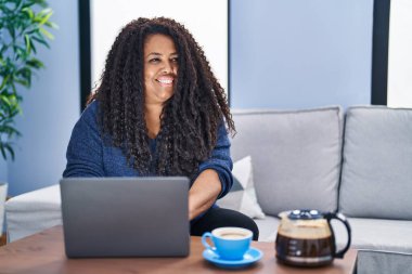 African american woman using laptop drinking coffee at home