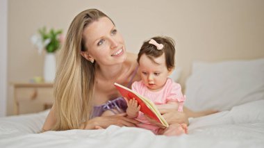 Anne ve kızı yatak odasında kitap tutarak yatıyorlar.