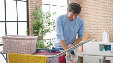 Genç İspanyol adam gülümsüyor. Çamaşır odasında kendine güveni tam bir elbise asıyor.