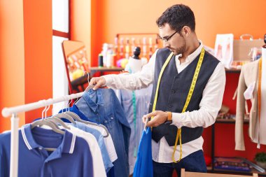Genç İspanyol terzi atölyedeki askıda giysileri tutuyor.