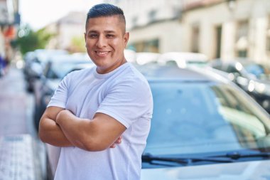 Young latin man smiling confident standing with arms crossed gesture at street
