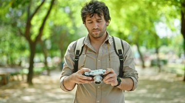 Sırt çantası takan İspanyol bir turist parkta ciddi yüzlü bir kamera tutuyor.