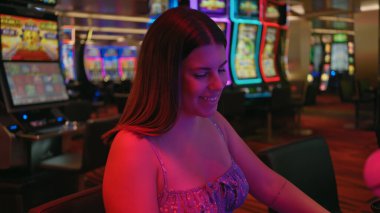 Neşeli bir kumarhanede kumar makinesinde oynayan gülümseyen genç bir İspanyol kadın.