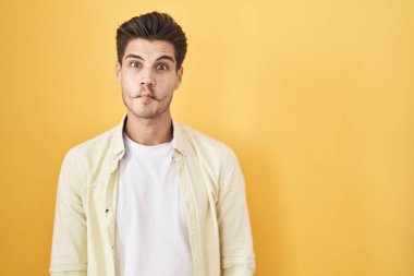 Sarı arka planda duran İspanyol genç adam dudaklarıyla balık suratı yapıyor, çılgınca ve komik bir jest. Komik ifade. 
