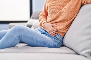 Evdeki kanepede oturan güzel İspanyol kadın mide ağrısı çekiyor.