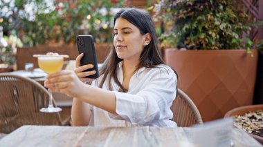 Genç ve güzel İspanyol bir kadın barın terasında tropik bir kokteyl içkisine fotoğraf çekiyor.