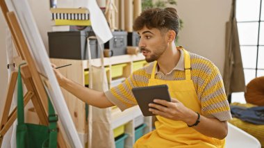 Yakışıklı genç Arap sanatçı bir sanat stüdyosundaki dokunmatik tablosuna kendini tamamen kaptırmış ve yaratıcılığını en sevdiği tuvale yansıtmış.