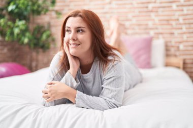 Young beautiful plus size woman smiling confident lying on bed at bedroom
