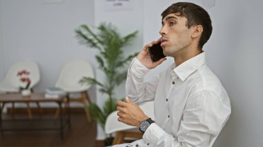 Yakışıklı, genç İspanyol bir adam, başarılı bir profesyonel, akıllı telefonuyla rahat bir sohbete dalmış, kapalı bir bekleme odasının koridorunda rahat bir şekilde oturuyor.