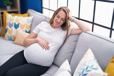 Young pregnant woman touching belly sitting on sofa at home