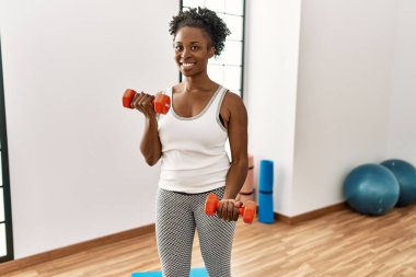 Spor merkezinde dambılları kullanarak gülümseyen Afrikalı Amerikalı kadın.