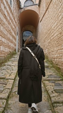 Topkapı Sarayı 'nın tarihi sahnesinde asfalt bir sokakta yürüyen esmer bir kadının arka görüntüsü, İstanbul.