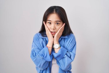 Beyaz arka planda duran genç Çinli kadın korkmuş ve şok olmuş, şaşırmış ve şaşırmış bir halde. 