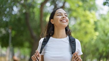 Afro-Amerikalı turist, parkta sırt çantası takıp gülümsüyor.