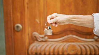 Olgun bir kadının ev anahtarlarını ahşap bir kapının önünde tutması yeni bir ev sahibi olduğunu gösterir..