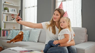 Kafkasyalı anne ve kız, iç açıcı doğum günü anıları yaşatıyorlar, sarılıyorlar ve akıllı bir telefonla büyüleyici bir fotoğraf çekiyorlar, rahat oturma odasındaki kanepeden..
