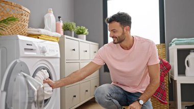 Çamaşır odasında kendine güvenen genç İspanyol adam gülümsüyor.