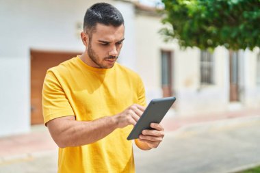 Latin kökenli genç bir adam sokakta ciddi bir ifadeyle dokunmatik ped kullanıyor.