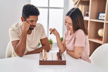 Man and woman couple sitting on table playing chess at home