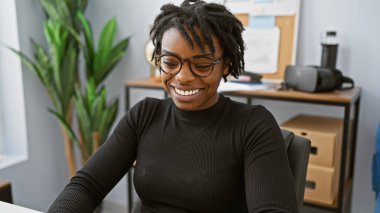 Ofisinde rastalı saçları olan, bilgisayar ekranına bakan neşeli siyah bir kadının portresi..