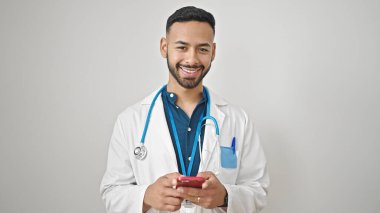 Genç İspanyol doktor, izole edilmiş beyaz arka plan üzerinde akıllı telefon kullanarak gülümsüyor.