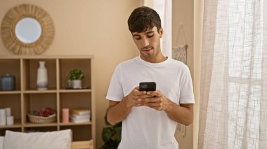 Young hispanic man using smartphone at home